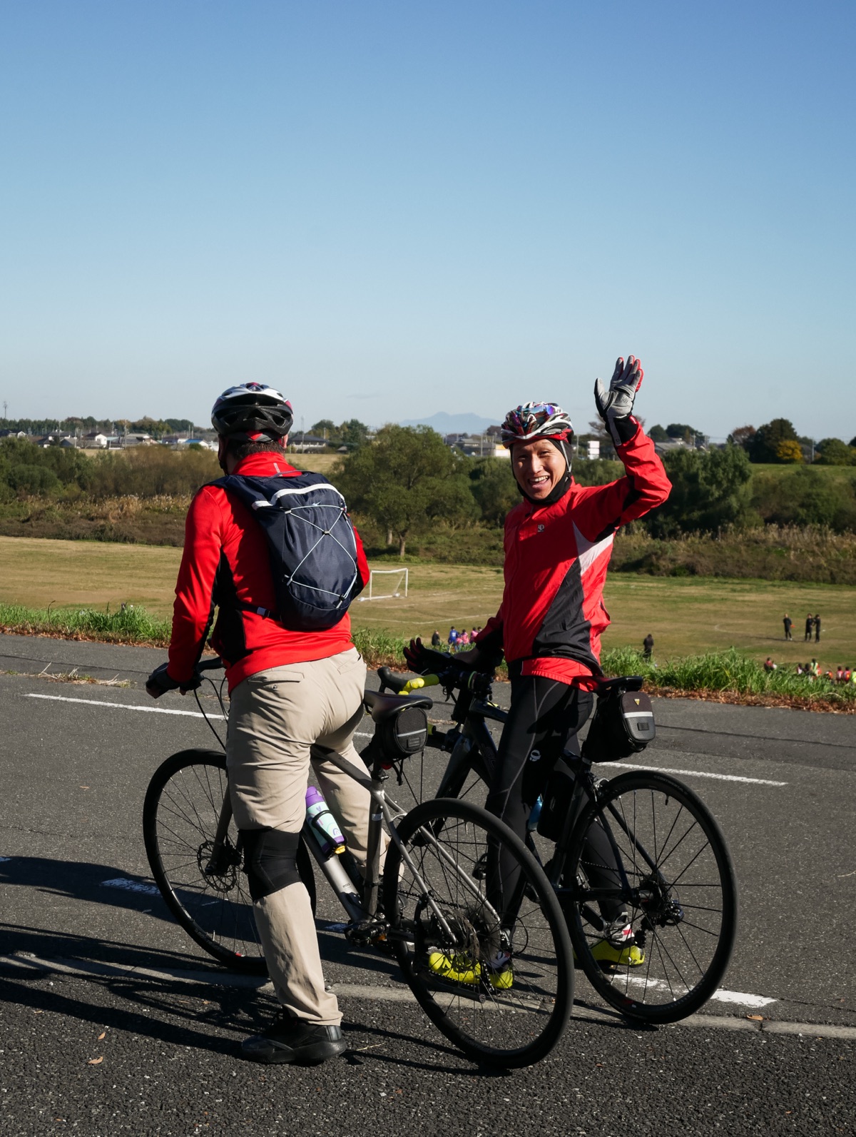 Two cyclists on a riverside path, one waving